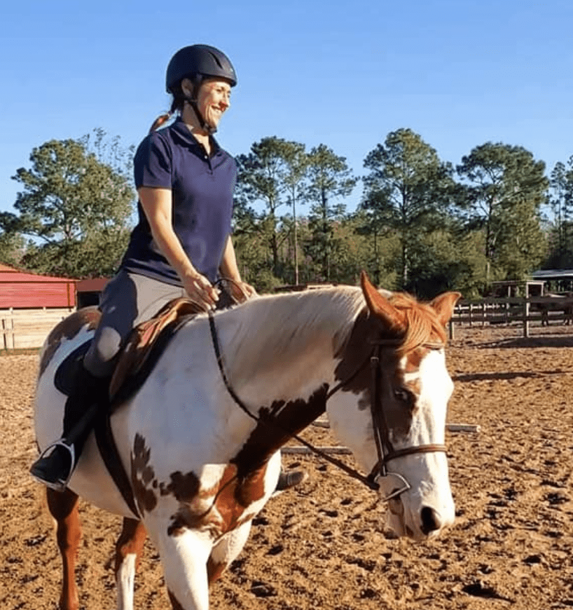 An adult lesson student is smiling ear to ear while riding a paint horse English