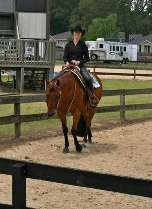 Samantha Edgin is riding Bo in a Western show. She is smiling at the camera while riding one handed in black attire.