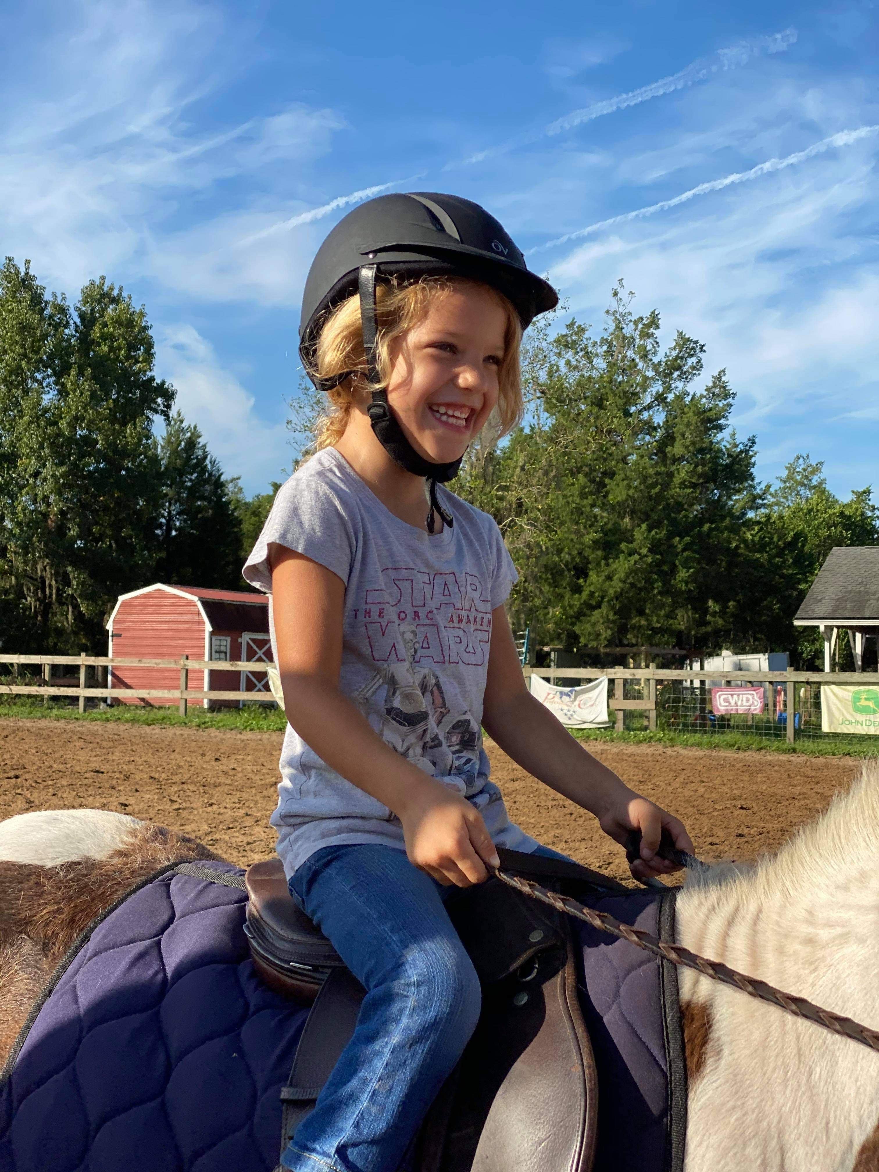 Young 4 year old student smiling on the back of a pony during lessons.