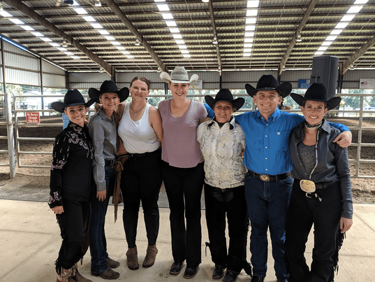 Seven members of the UNF Western team standing together smiling in a covered arena during a show